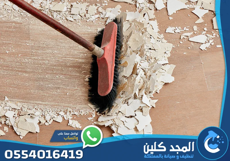 تنظيف بعد التجديد الرياض 0554016419 المجد كلين مشهد علوي يظهر كنس بقايا طلاء أو جبس متكسر من على أرضية خشبية بفرشاة حمراء.