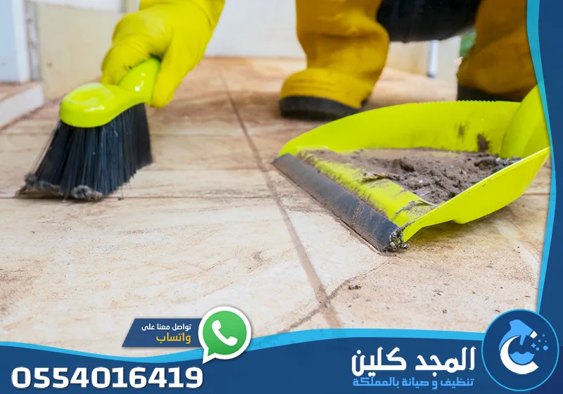 تنظيف عميق بعد التشطيب الرياض 0554016419 المجد كلين يد ترتدي قفازاً أصفراً تستخدم فرشاة ومجروداً لجمع المخلفات الدقيقة من فوق البلاط.